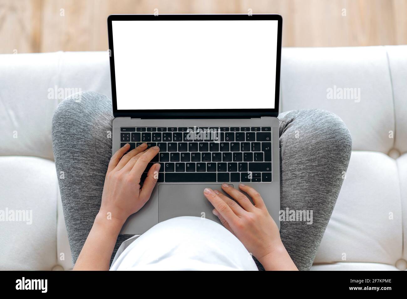 Gadget wireless, concetto di tecnologia. Vista dall'alto della donna incinta in una t-shirt bianca seduta sul divano, tenendo un computer portatile con schermo bianco vuoto in mano, posto per la vostra presentazione Foto Stock