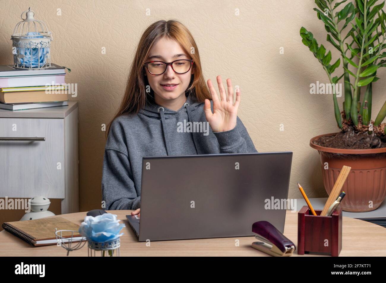 bella ragazza adolescente con occhiali si trova di fronte ai computer portatili. La ragazza adolescente ondeggia la mano sullo schermo del portatile. Concetto di comunicazione remota con frie Foto Stock