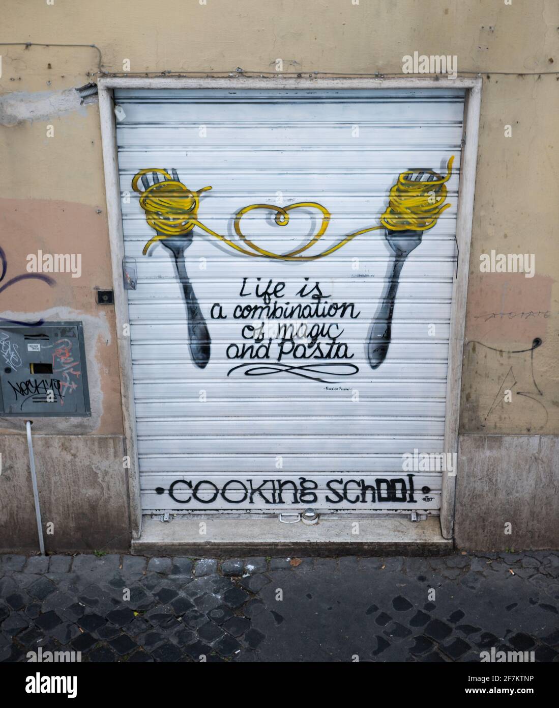 Graffiti d'arte di strada a Roma con due forchette e tagliatelle di pasta che formano un cuore al centro. Ispirata alla citazione Fellini 'la vita è una combinazione di magia Foto Stock