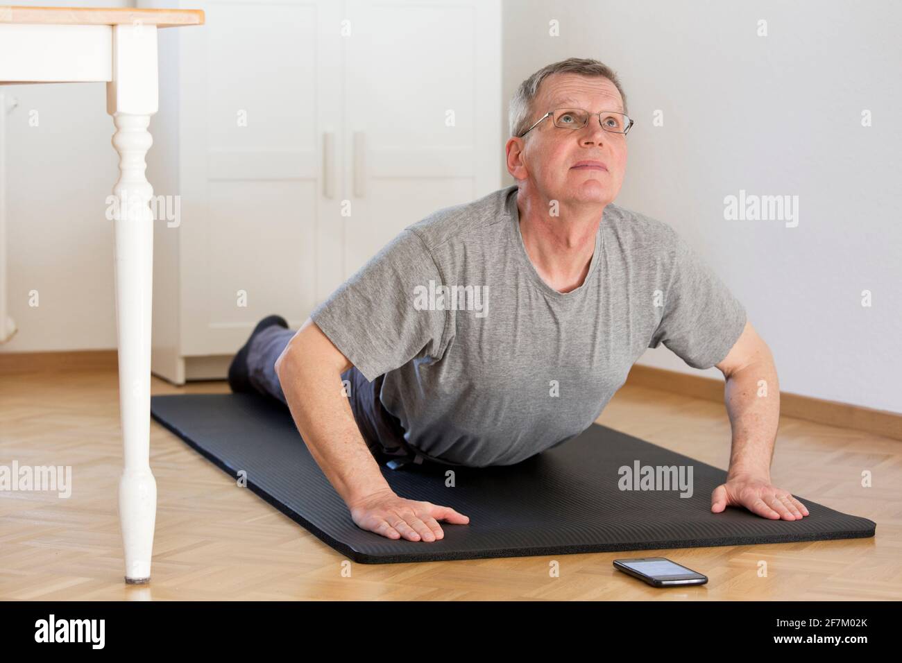 Uomo maturo che fa yoga a casa con smartphone in davanti a lui - fuoco selettivo sul viso Foto Stock