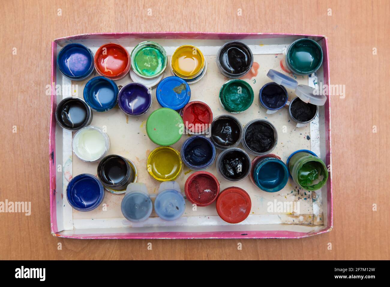 Una scatola con vecchi vasi aperti di gouache per la pittura. Vista dall'alto di vasi semidisvuoti di pitture di gouache. Disposizione piatta sul tavolo. Foto Stock