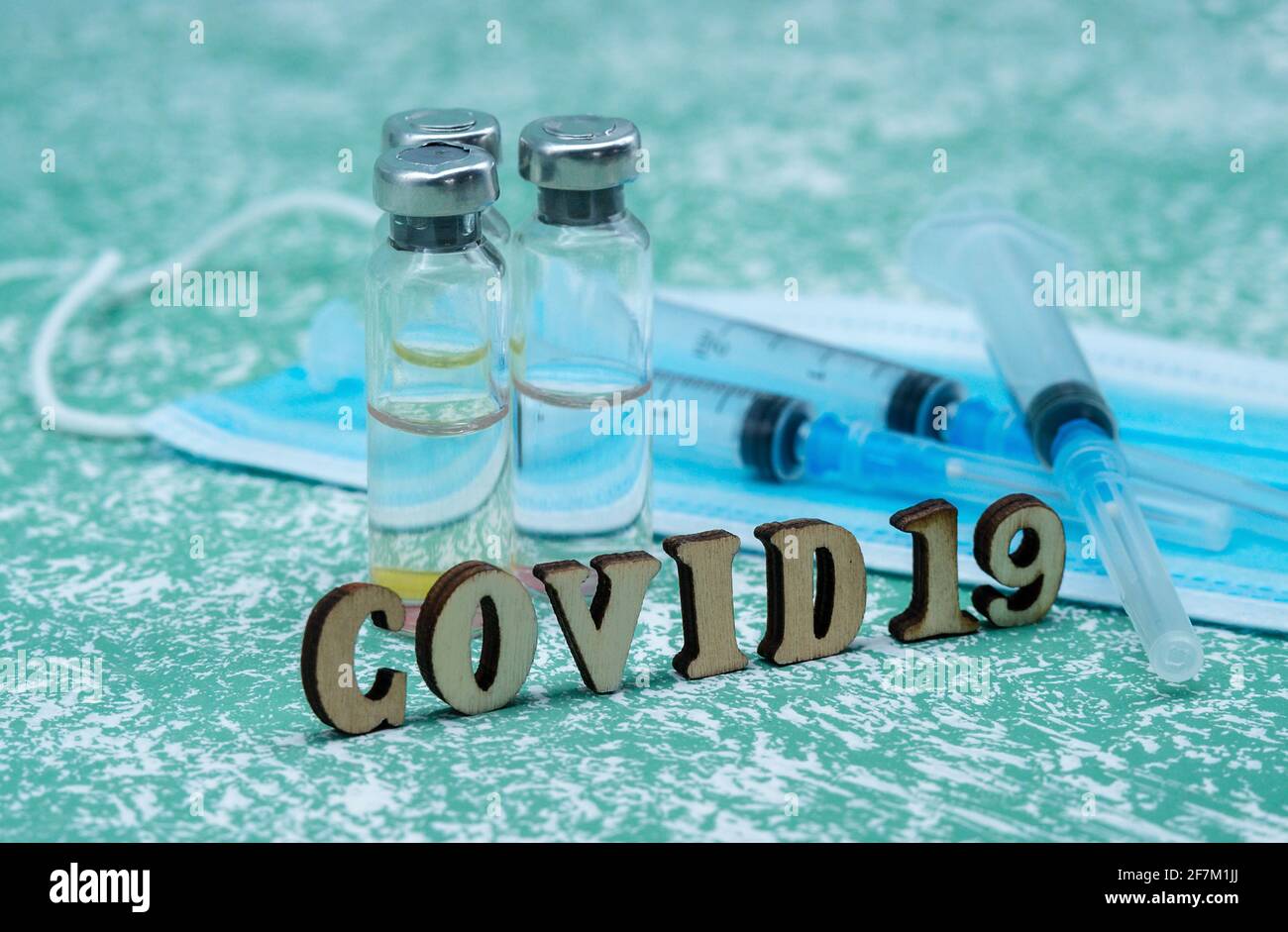 Prevenzione delle malattie stagionali. Fiale mediche, siringhe e una maschera su sfondo verde. Vaccinazione contro covid-19. Foto Stock