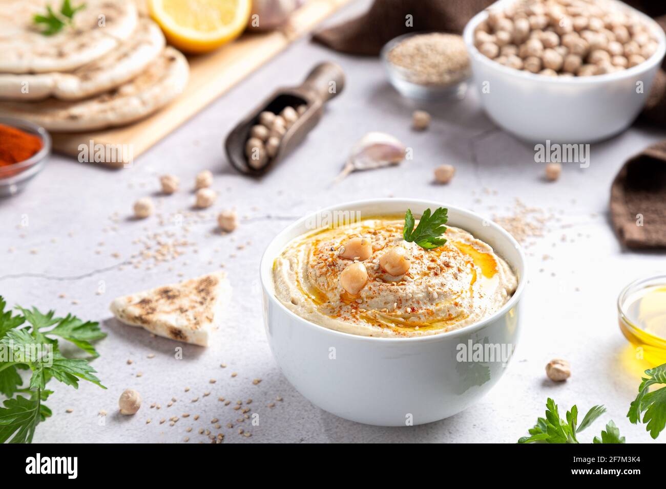 Hummus classico in una ciotola con ingredienti su sfondo chiaro. Foto Stock