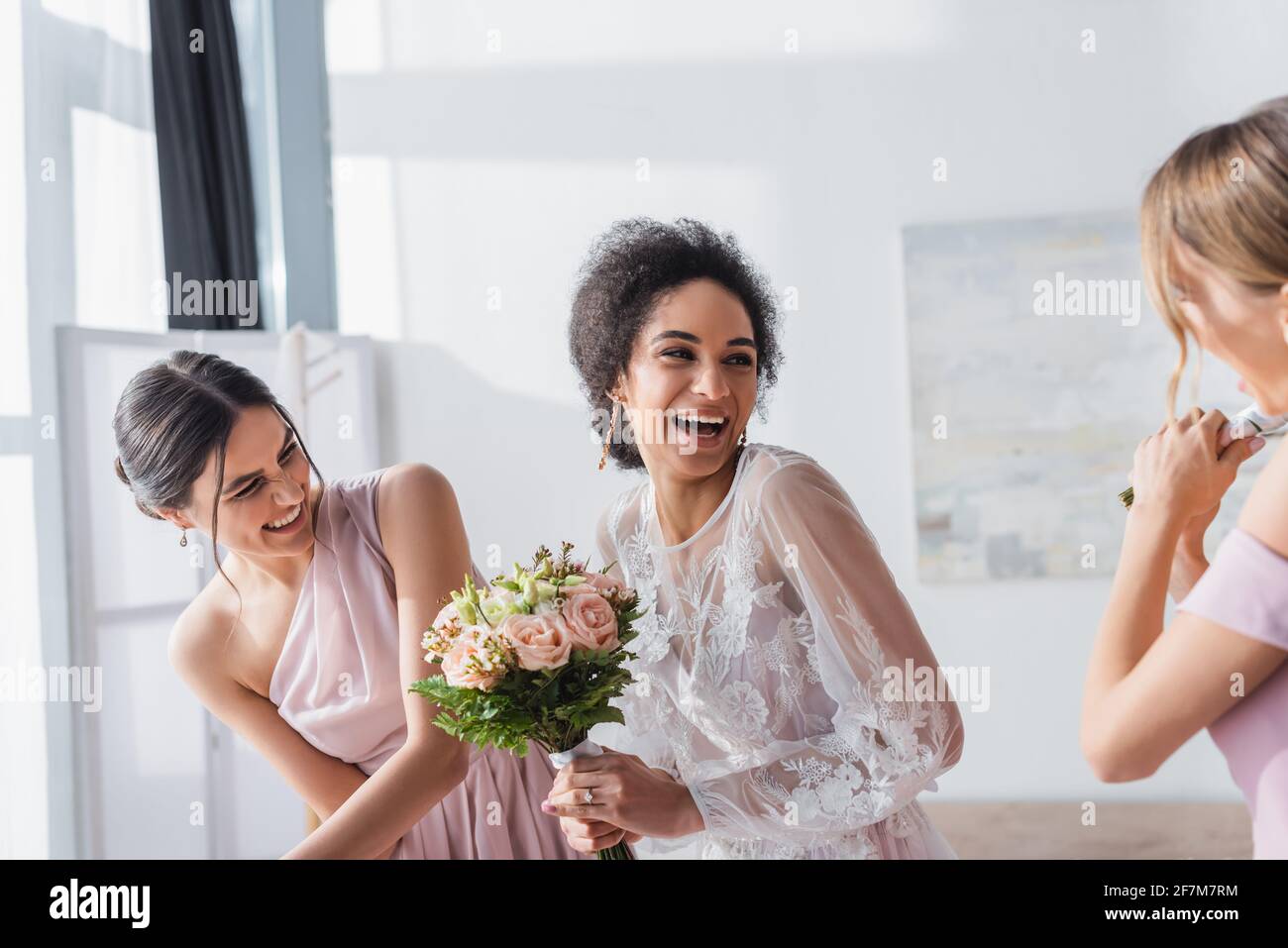 bride afroamericana eccitata che tiene il bouquet di nozze e ridendo vicino bridesmaid Foto Stock