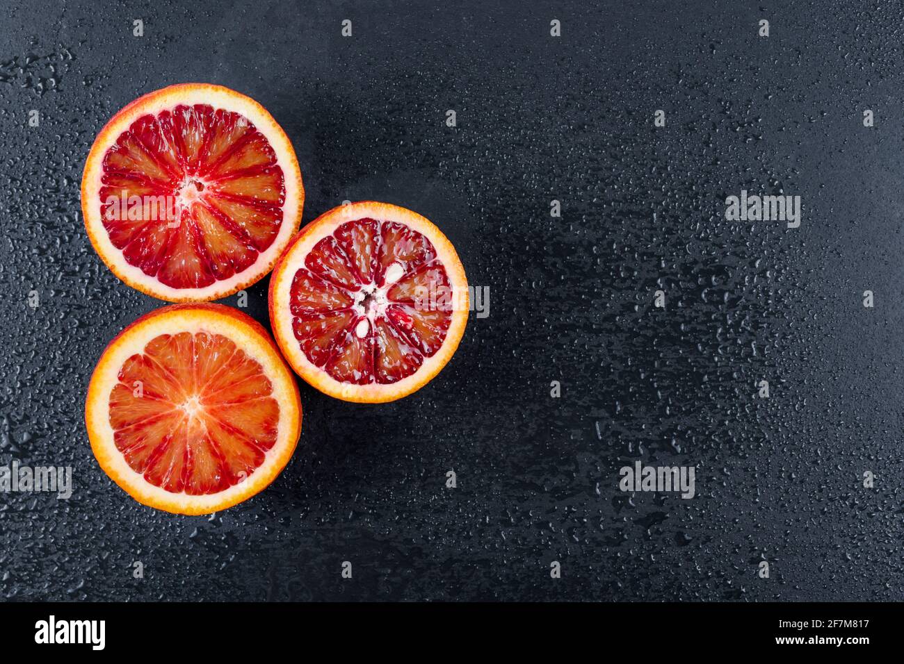 Arance sanguinose tagliate a metà su tavola di ardesia nera con gocce d'acqua. Arancio siciliano rosso. Vista dall'alto, spazio libero per il testo. Foto Stock