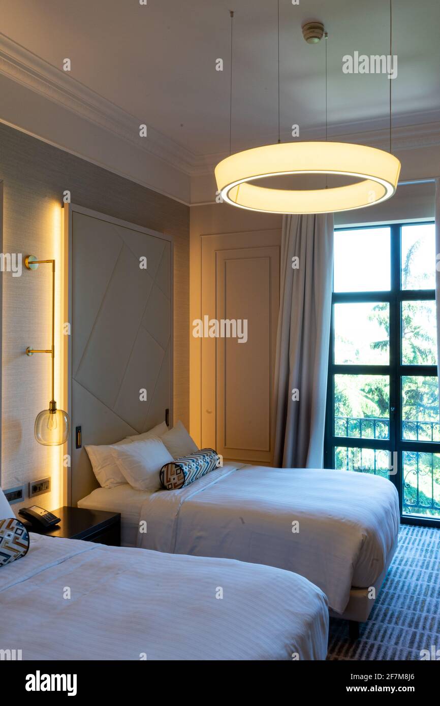 Una lussuosa camera da letto a due letti con biancheria da letto e biancheria bianca fresca negli interni moderni, sotto la lampada rotonda gialla Foto Stock