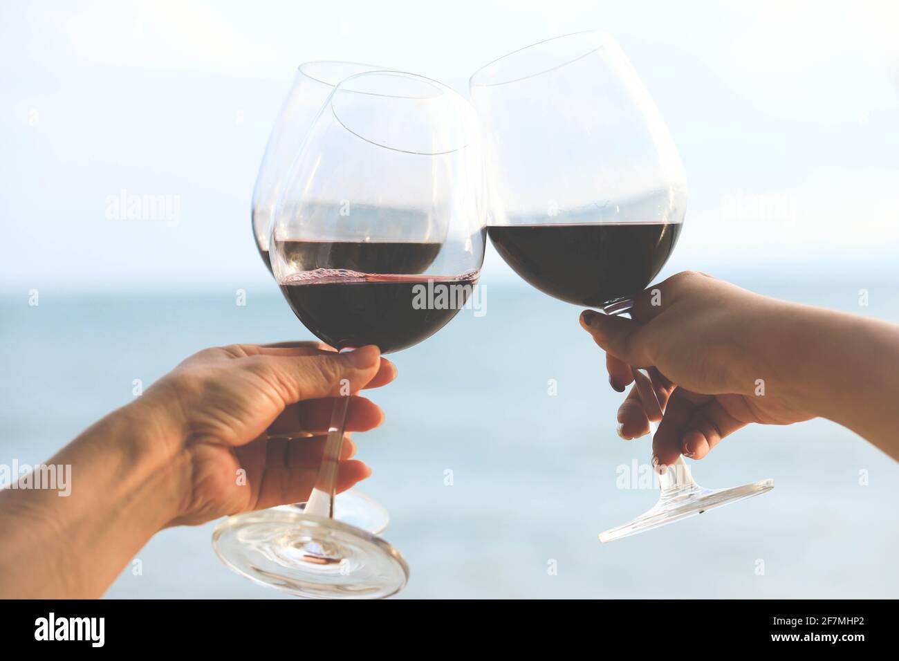 Primo piano su mani che tengono bicchieri di vino rosso sulla spiaggia, concetto di celebrazione Foto Stock