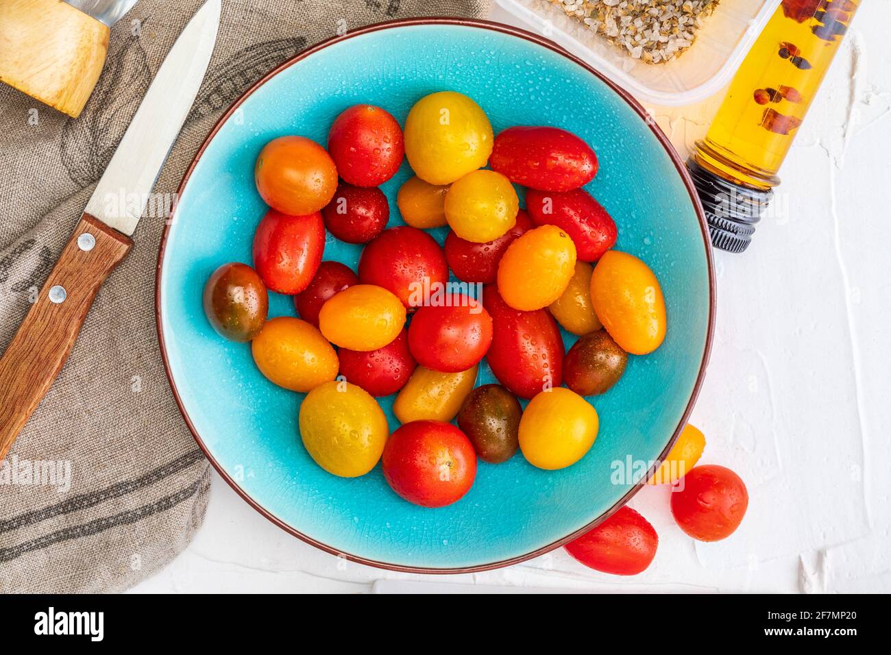 Ciotola di pomodori ciliegini colorati (rosso, granato e giallo), freschi e crudi. Con gocce d'acqua apparenza fatta in casa con olio d'oliva e spezie. Vista dall'alto Foto Stock