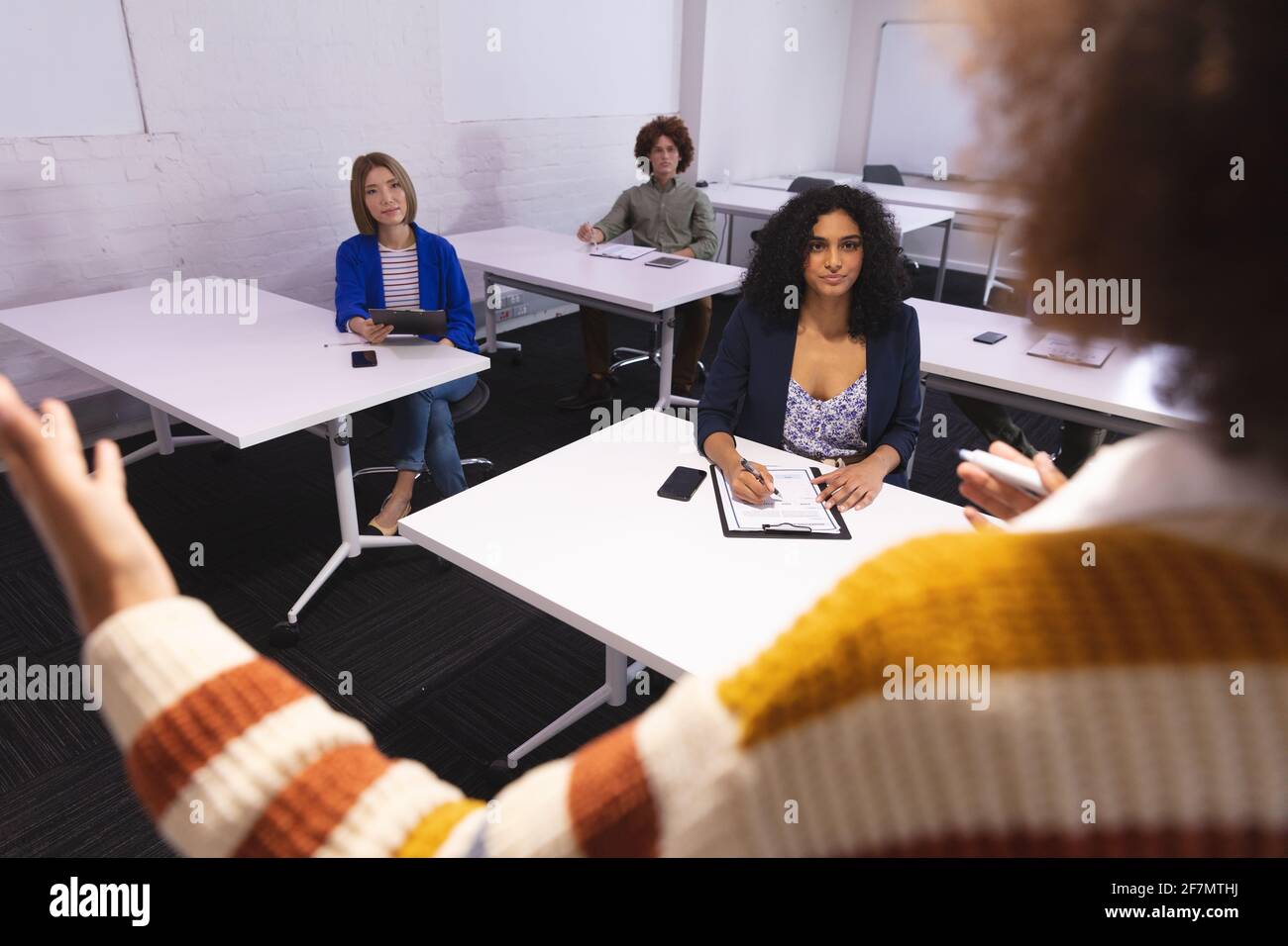 Diversi gruppi di colleghi di lavoro creativi in sala riunioni che ascoltano presentazione prendendo appunti Foto Stock