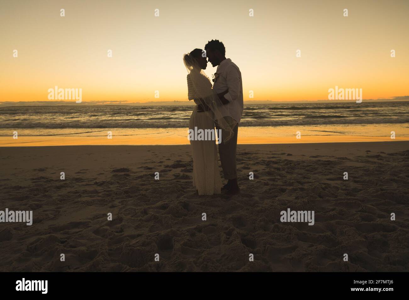 Felice coppia afroamericana in amore sposarsi, abbracciando sulla spiaggia durante il tramonto Foto Stock