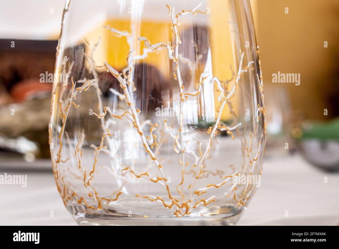 Primo piano di un calice da vino senza stelo con viti dipinte in oro e argento ai suoi lati. Siede vuoto su un tavolo finemente decorato in attesa di una festa. Foto Stock