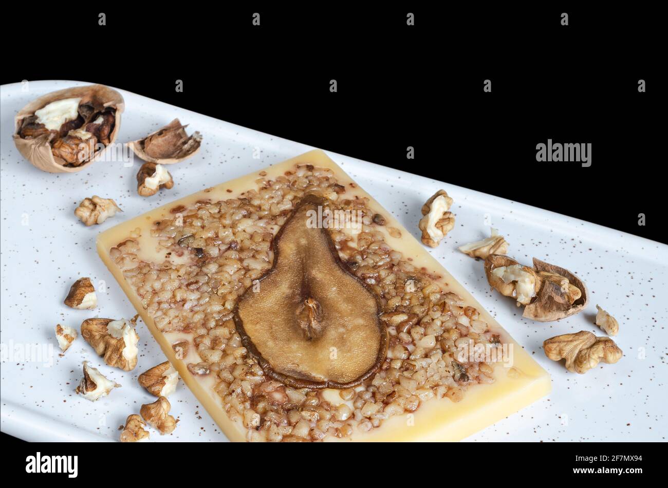 Formaggio da dessert con pere e noci tritate, su un tagliere. Messa a fuoco selettiva, sfondo nero Foto Stock