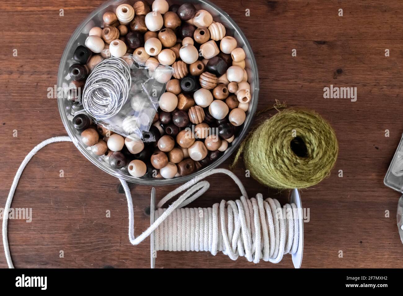 Una pila di perle di legno assortite, spago verde e corda di iuta di macrame arrotolata su una scrivania di legno duro in Ontario, Canada, febbraio 2021. Foto Stock