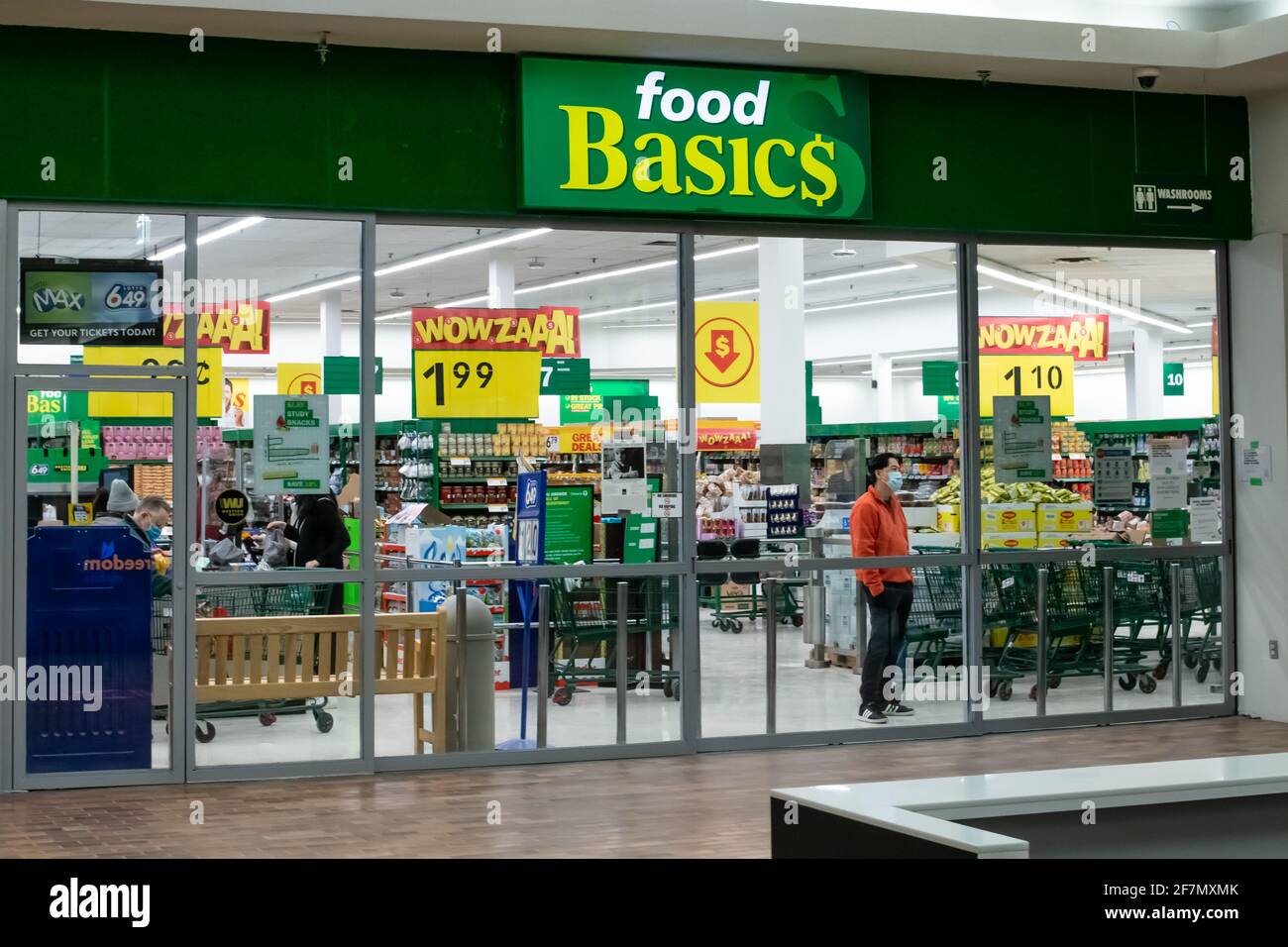 Londra, Ontario, Canada - 1 marzo 2021: Un uomo che indossa una maschera chirurgica usa e getta all'interno di un negozio di alimentari di base allo Sherwood Forest Mall. Foto Stock