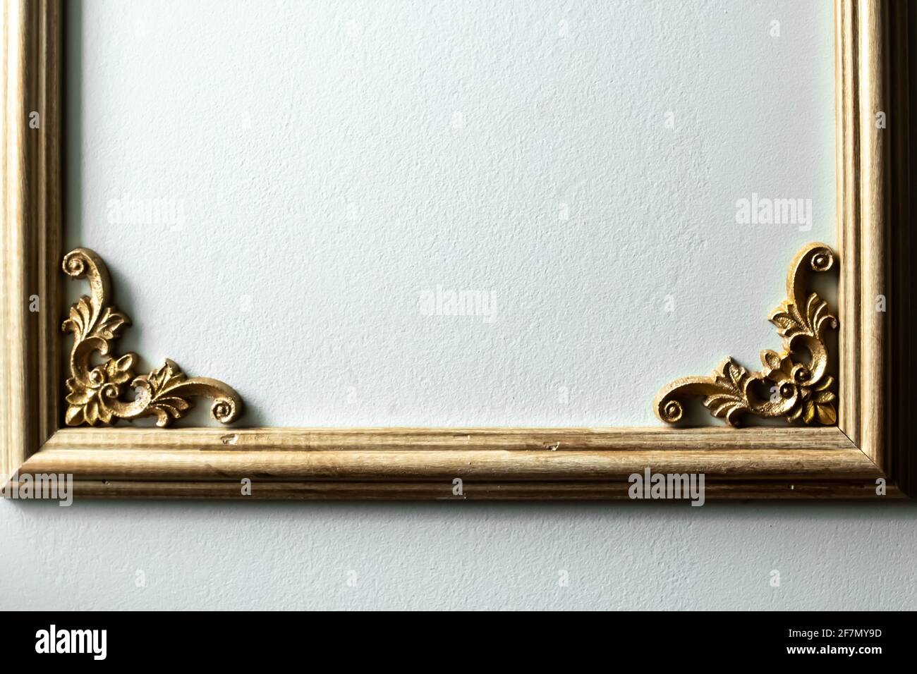 Closeup di una cornice in legno dipinto d'oro con un motivo floreale nell'angolo contro una parete verde pallido. Design ispirato alla classica francese romantica. Foto Stock