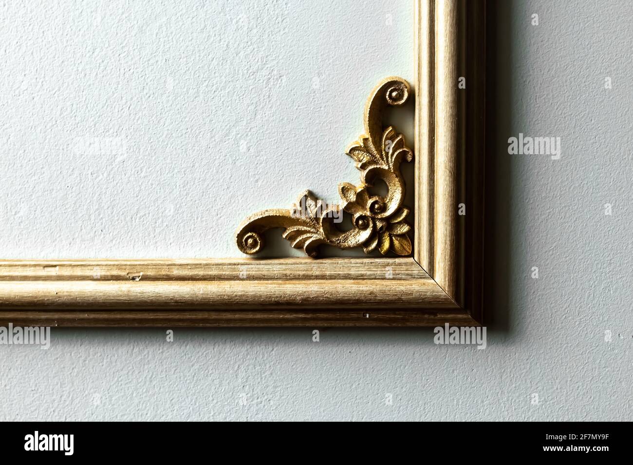 Closeup di una cornice in legno dipinto d'oro con un motivo floreale nell'angolo contro una parete verde pallido. Design ispirato alla classica francese romantica. Foto Stock