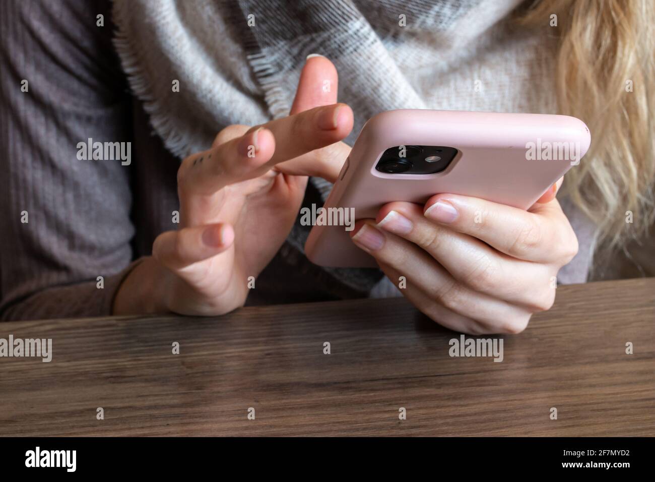Donna con un tatuaggio delle dita e capelli biondi che scorrono rapidamente sul suo smartphone rosa in un bar, febbraio 2021. Foto Stock