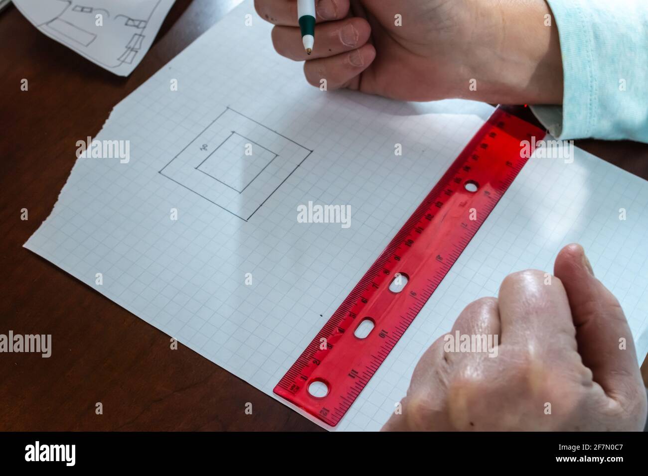 Una donna usa una penna per contare le misure e tracciare una pianta per una casa su carta grafica quadrata usando un righello rosso chiaro sulla scrivania di legno duro. Foto Stock