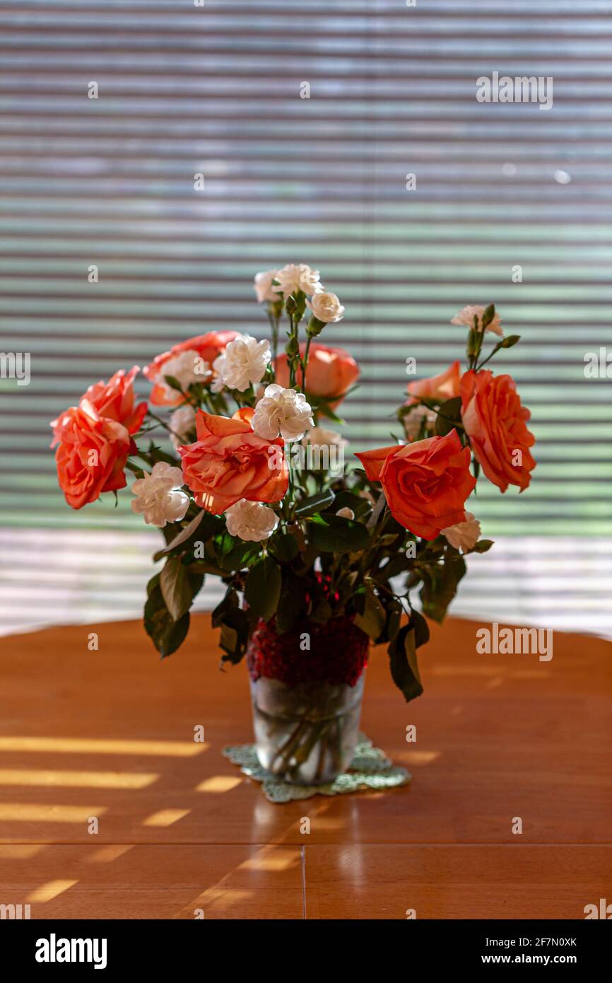 Fiori, rose e garofani in un vaso vicino a una finestra Foto Stock