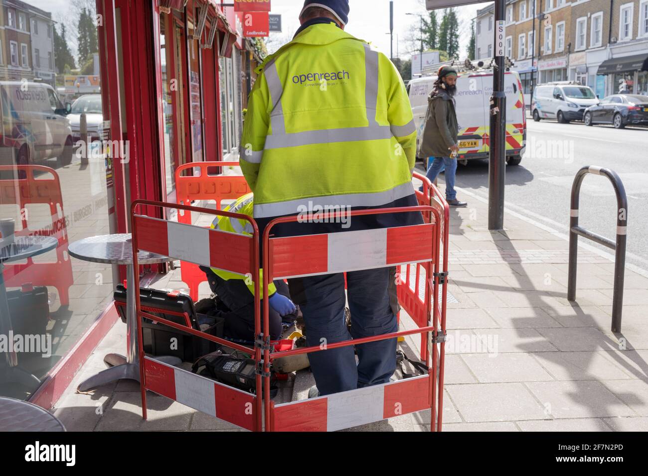 L'ingegnere Openreach si trova accanto ai suoi colleghi al lavoro, collegando nuove linee all'interno della scatola dei cavi sotto il marciapiede, barriera di sicurezza stradale, Londra Foto Stock
