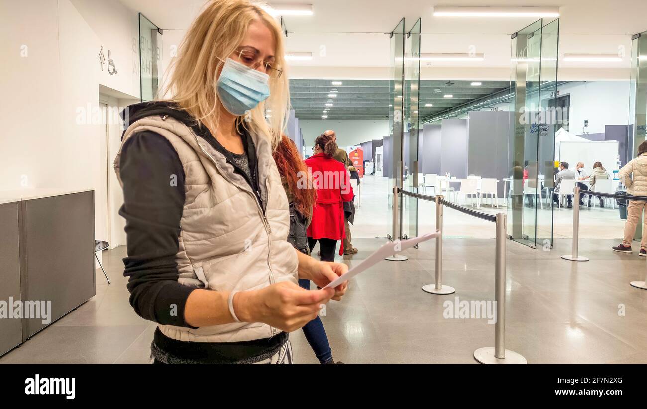 Bologna, Italia - Aprile 2021: Coda di donne con maschere chirurgiche nel centro di vaccinazione italiano per essere vaccinate per la vaccinazione europea COVID-19 Foto Stock