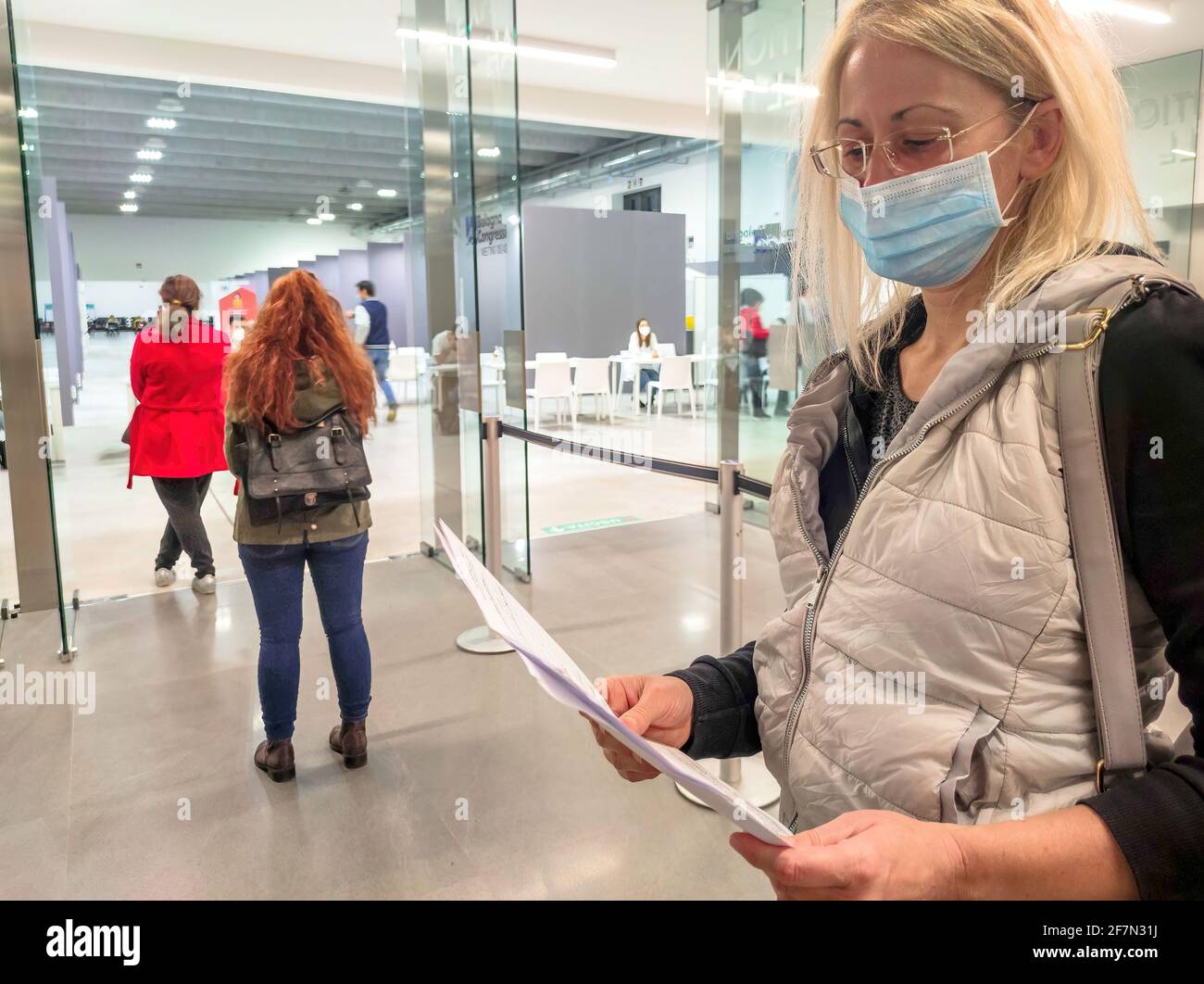 Bologna, Italia - Aprile 2021: Coda di donne con maschere chirurgiche nel centro di vaccinazione italiano per la vaccinazione europea COVID-19 Foto Stock