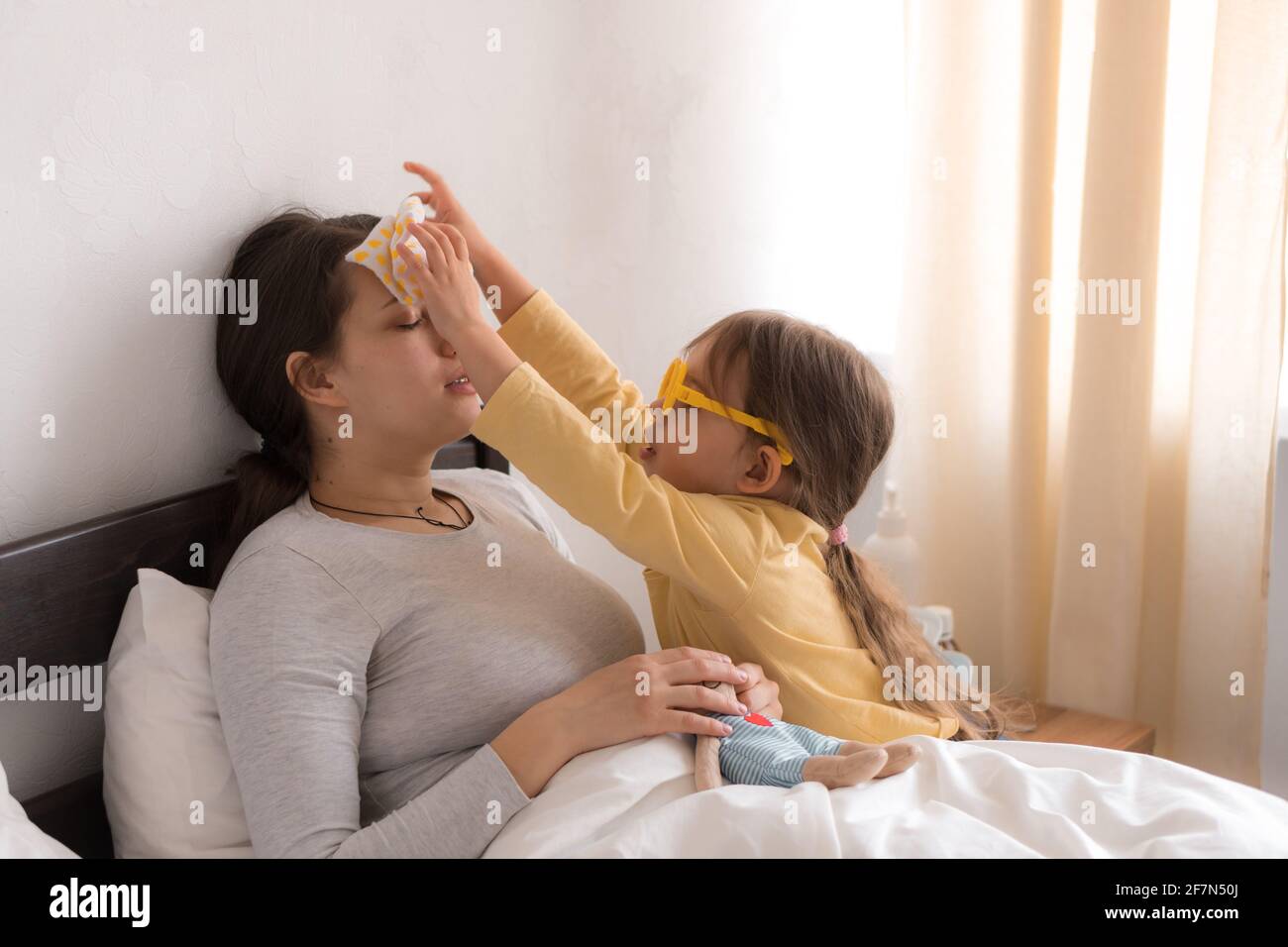 bambina che indossa un medico che gioca in uniforme, infermiera con mamma giovane, pannaia in camera da letto, controllo della gola della madre, misura la temperatura, si prenda cura, famiglia Foto Stock