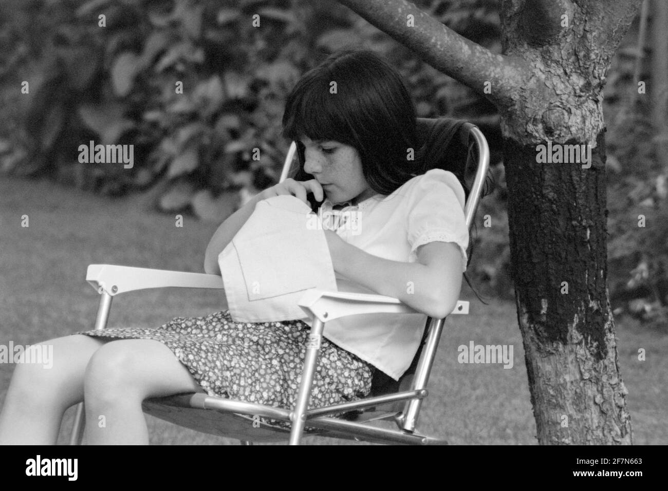 giovane ragazza che si concentra su cucire nel giardino early80 uk Foto Stock