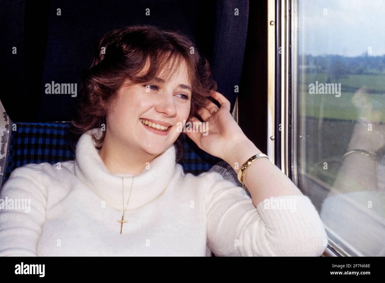 bella ben vestito sorridente giovane donna che guarda fuori treno finestra delle carrozze durante il viaggio verso la destinazione turistica all'inizio degli anni '80 inghilterra regno unito Foto Stock