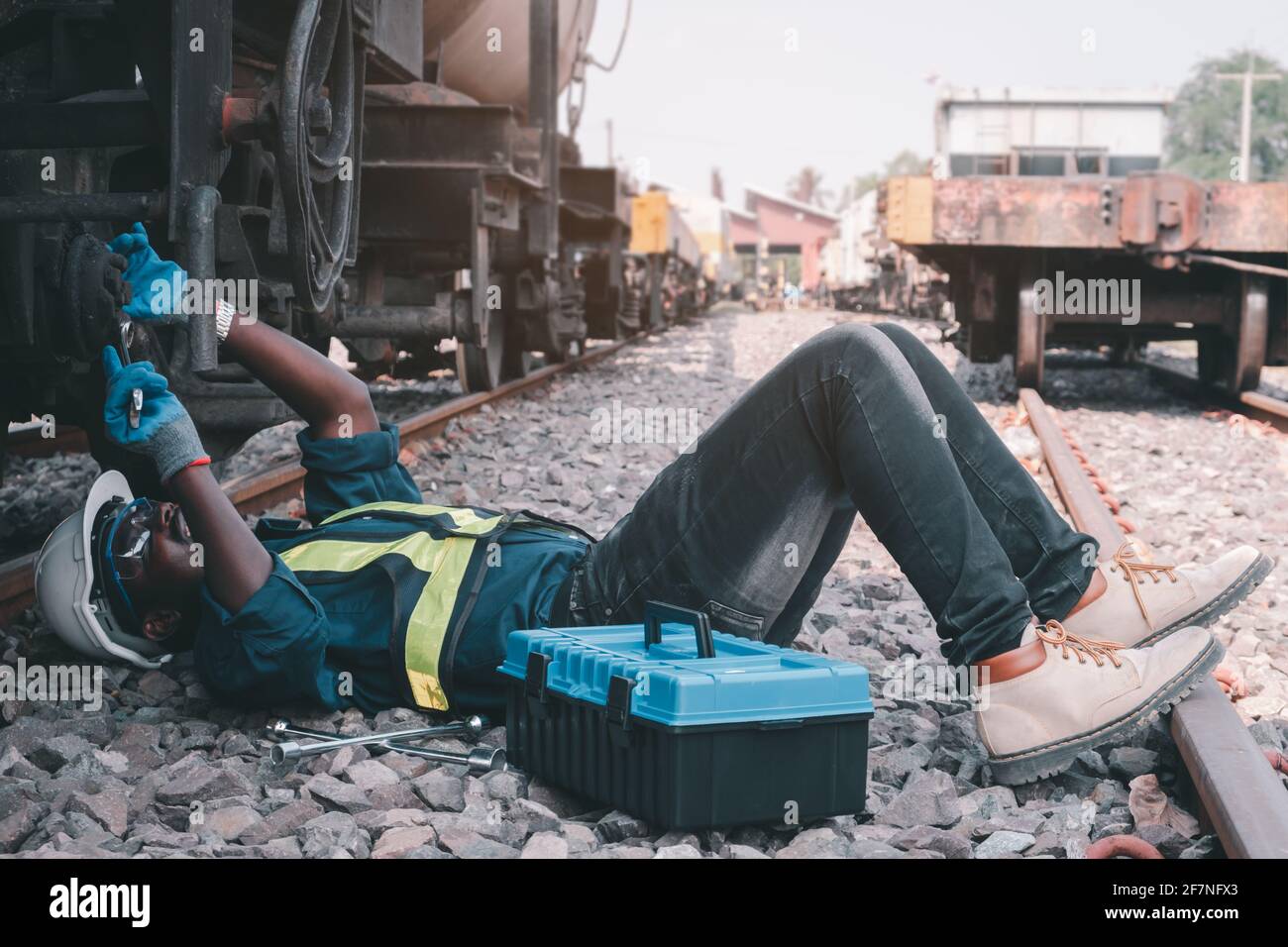 Un tecnico africano che indossa casco, boschetti e giubbotto di sicurezza utilizza una chiave per riparare il treno Foto Stock