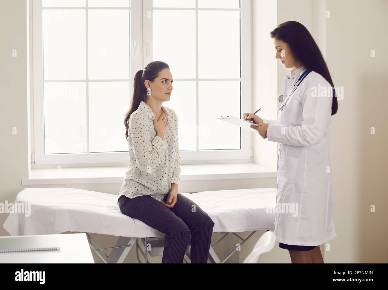 Donna che si lamenta di tosse e mal di gola seduta all'esame letto presso l'ufficio del medico Foto Stock