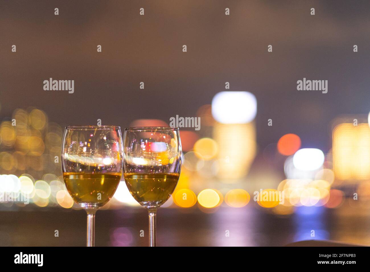 Due bicchieri di vino con scintillanti luci notturne della città in centro, Hong Kong Victoria Harbour come sfondo, concetto romantico per gli amanti e valente Foto Stock