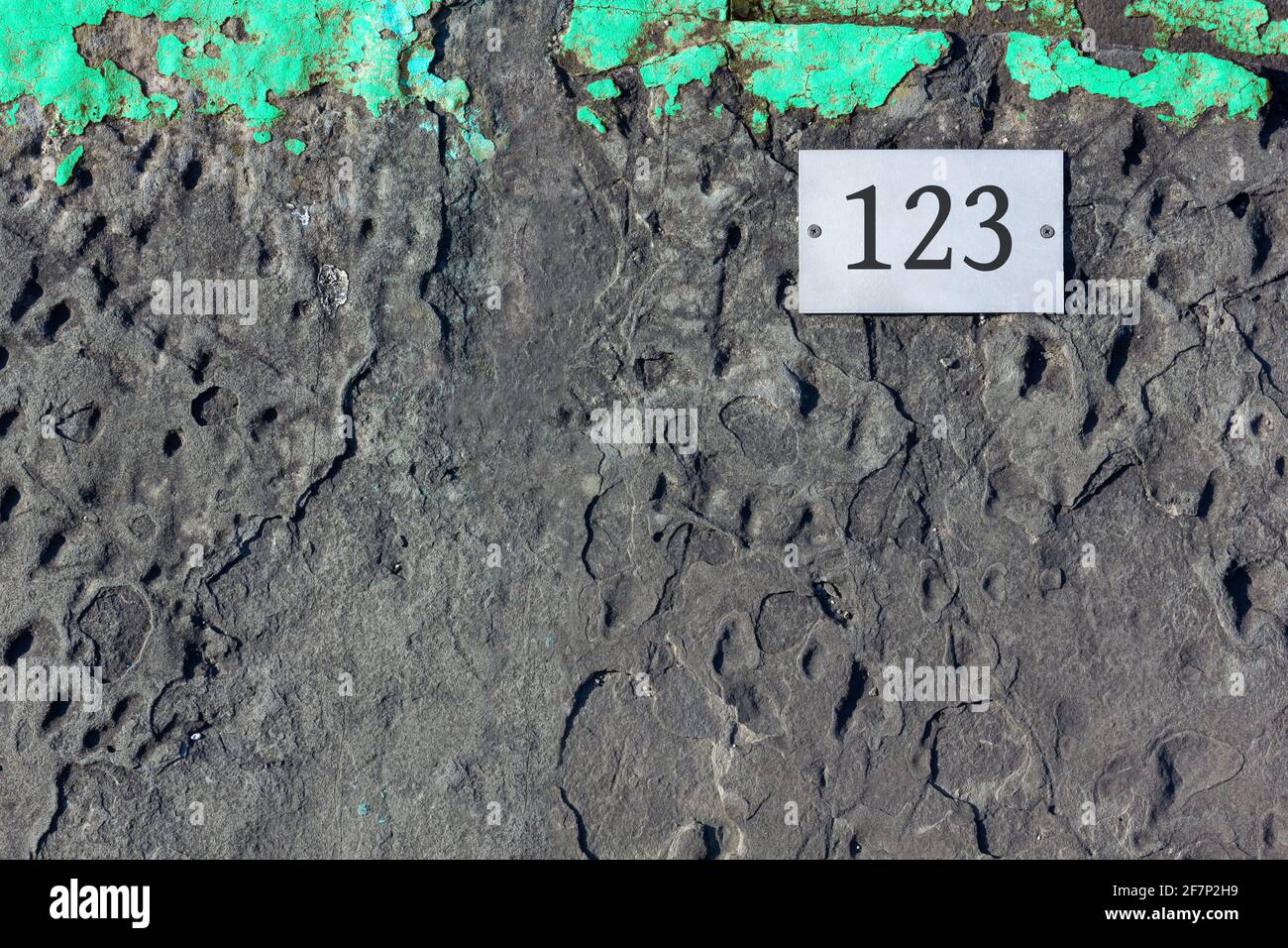 Fondo asfaltato con una striscia verde turchese sulla parte superiore e. una piastrella bianca avvitata con il numero 123 stampato su di essa Foto Stock