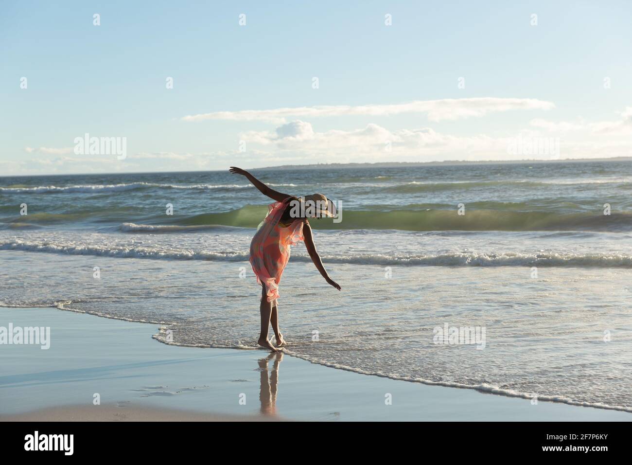 Donna mista da corsa con cappello di paglia che cammina lungo la riva del mare con mani sparse Foto Stock