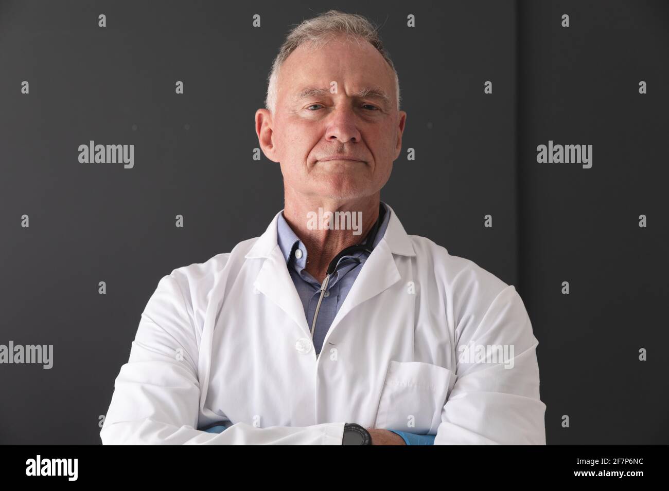 Ritratto di dottore caucasico di sesso maschile superiore con cappotto bianco in piedi con le braccia incrociate, sorridente Foto Stock