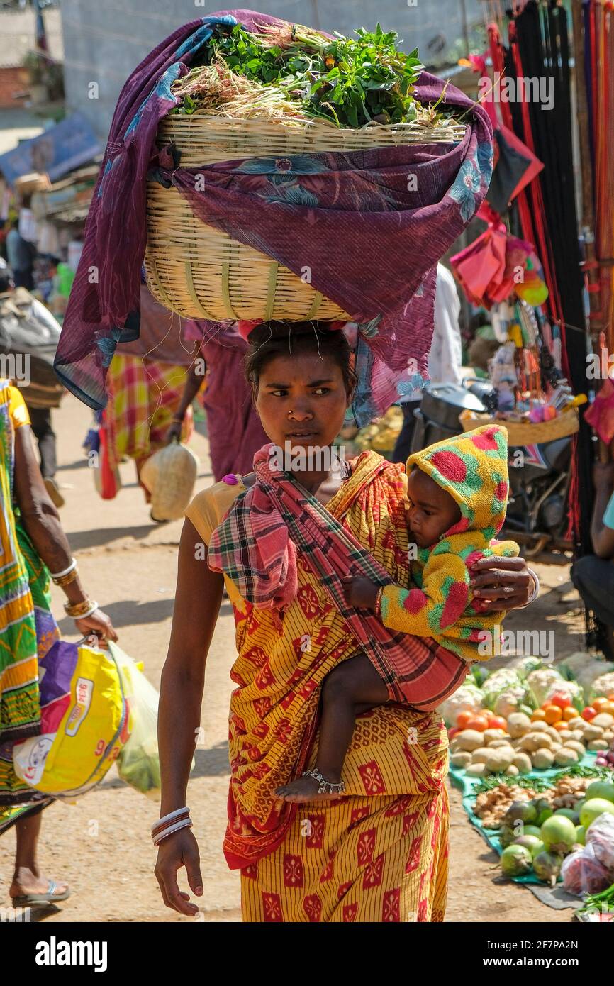 Koraput, India - Febbraio 2021: Donna Adivasi dalla tribù Kondh con il suo bambino che acquista verdure nel mercato Koraput il 21 febbraio 2021 in od Foto Stock