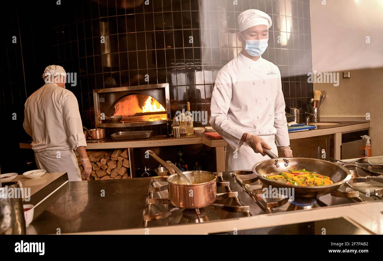 Cuoco asiatico che tiene i peperoni in padella sopra il bruciatore di stufa Foto Stock