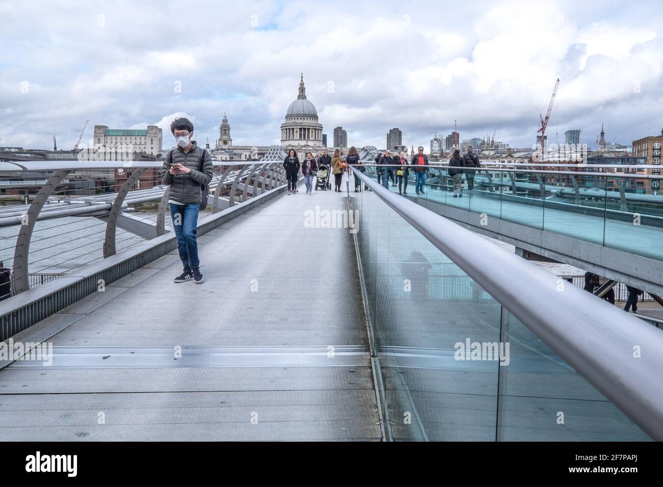 Londra, Inghilterra, Regno Unito - 15 marzo 2020 - persona che cammina sul Millennium Bridge indossando la maschera guardando il dispositivo del telefono cellulare Foto Stock