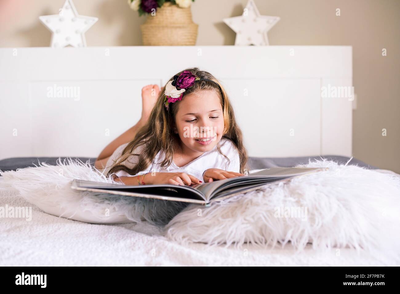La bambina legge un libro sul letto in una stanza luminosa. Il bambino si  trova nella camera da letto con un libro e studia con entusiasmo il libro.  Spazio libero per il