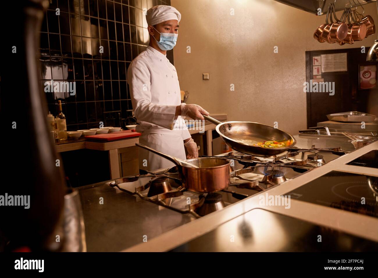 Cuoco asiatico inclinando una padella calda con le fette di verdure Foto Stock