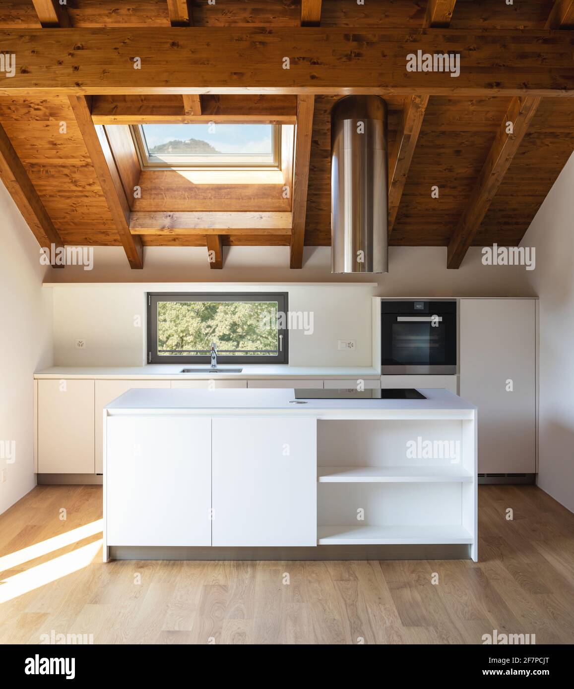 Vista frontale bianca cucina moderna con isola, cappa in acciaio e forno. Piccola finestra con vista sulla natura. Nessuno dentro. Foto Stock