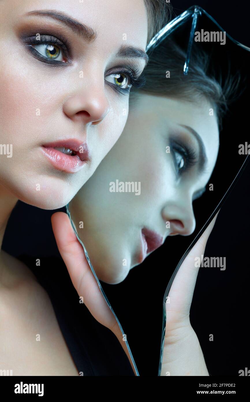 Ragazza con un bardo dello specchio. Femmina con specchio in mano che si posa su sfondo grigio. Riflessione del volto nella scheggia dello specchio. Foto Stock
