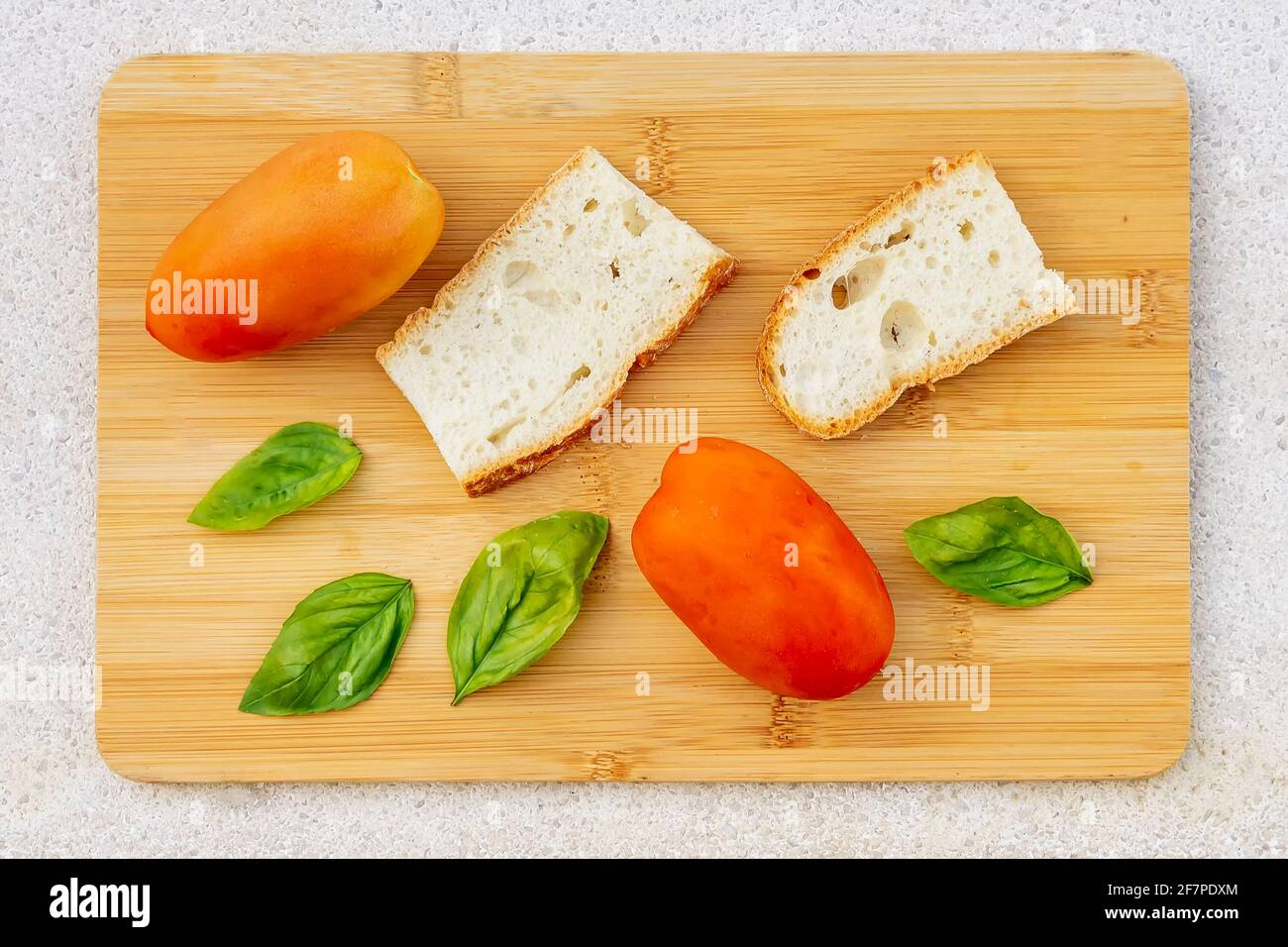 Gli ingredienti tipici di una gustosa bruschetta, pane, pomodori, foglie di basilico posti su un tagliere di legno Foto Stock