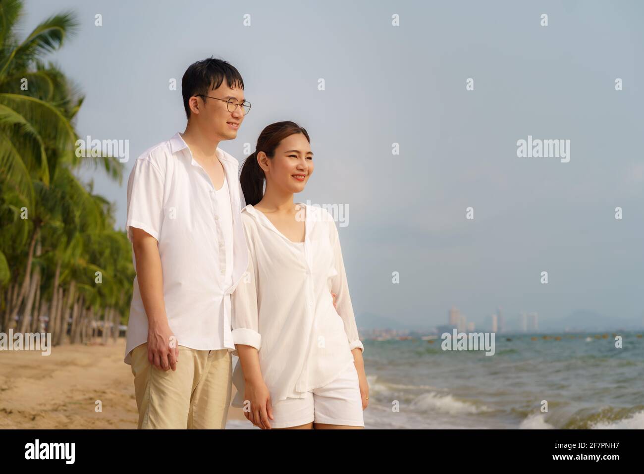La coppia asiatica cammina e si aggina su una spiaggia di mare con alberi di cocco mentre in vacanza in estate in Thailandia. Foto Stock