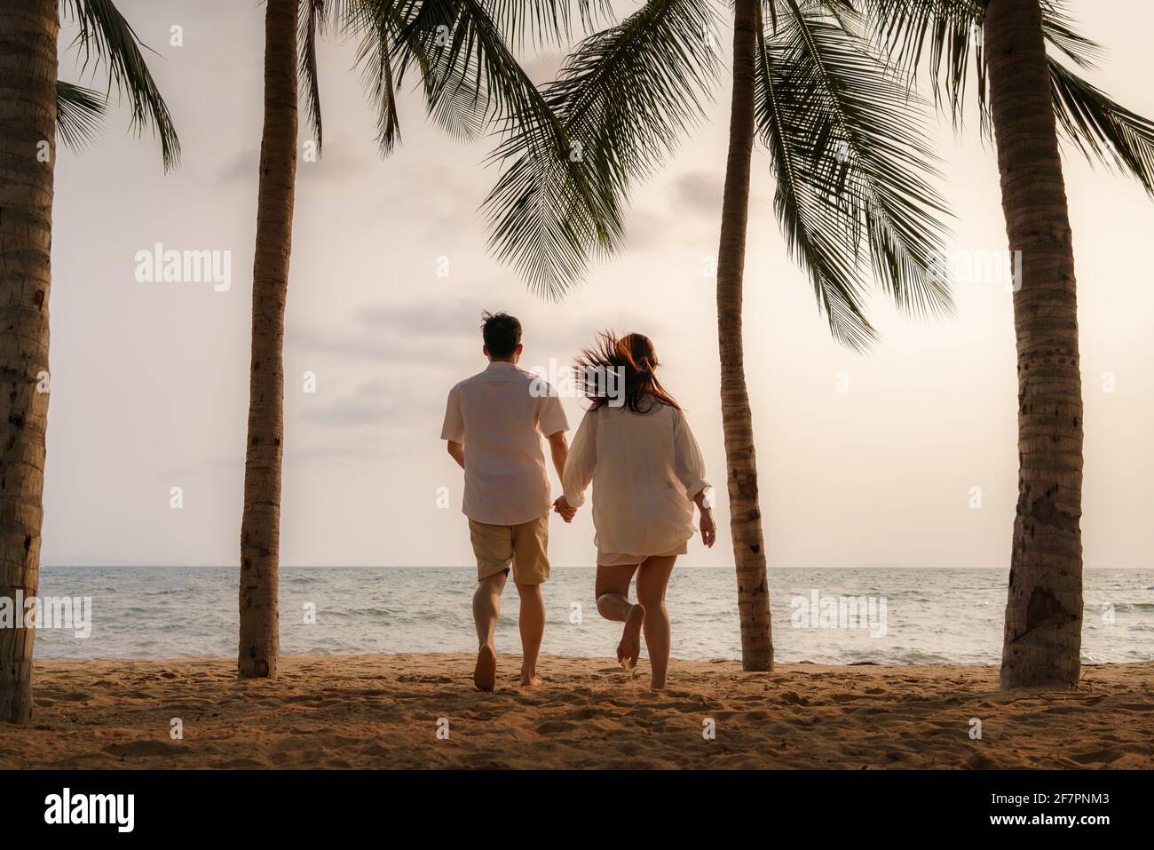 La coppia asiatica corre e tiene le mani su una spiaggia di mare con alberi di cocco mentre in vacanza in estate in Thailandia. Foto Stock