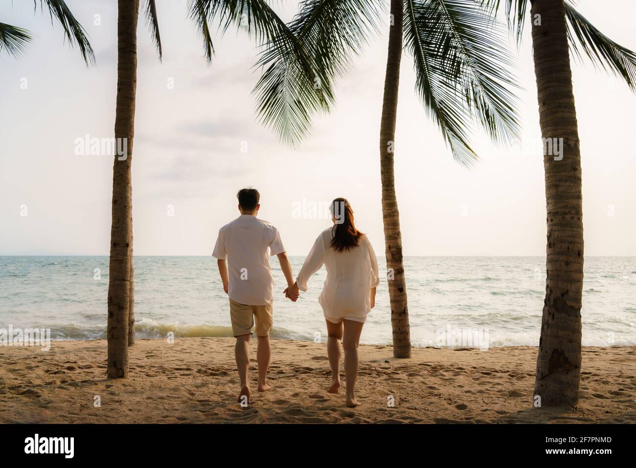 La coppia asiatica corre e tiene le mani su una spiaggia di mare con alberi di cocco mentre in vacanza in estate in Thailandia. Foto Stock