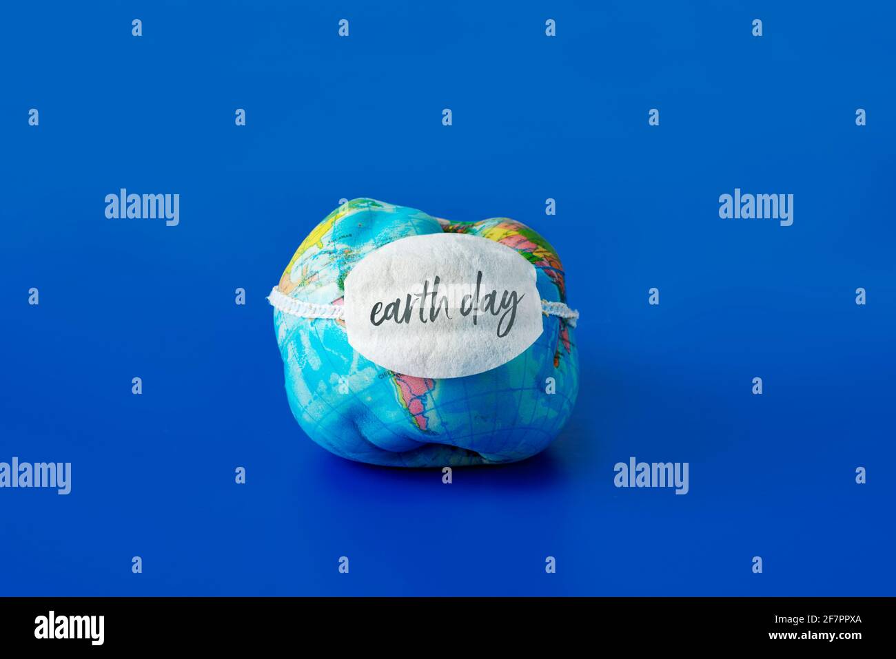 un globo di terra morbida deformato che indossa una maschera facciale con il testo giorno di terra scritto in esso, su uno sfondo blu Foto Stock