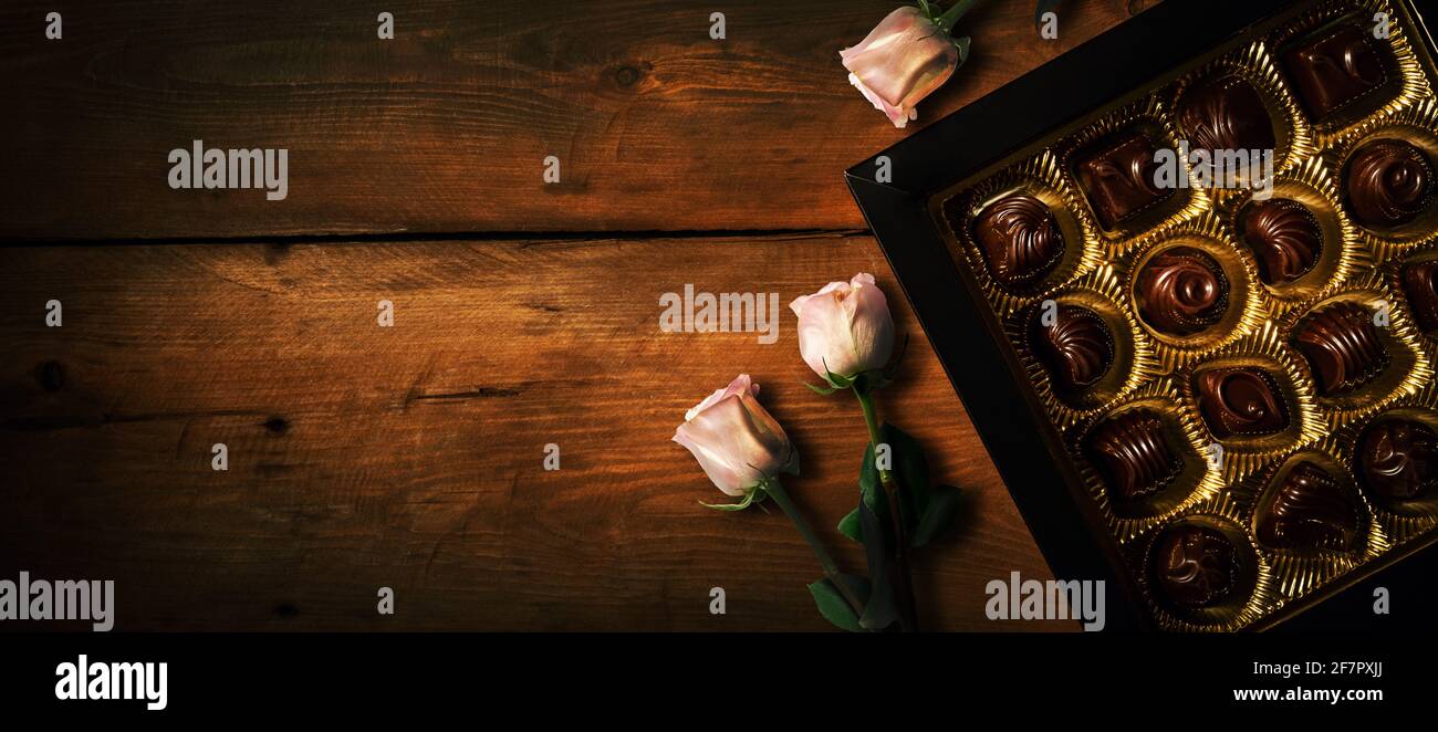 regalo romantico - scatola caramelle al cioccolato con fiori di rosa su vecchio sfondo di legno. spazio copia banner Foto Stock