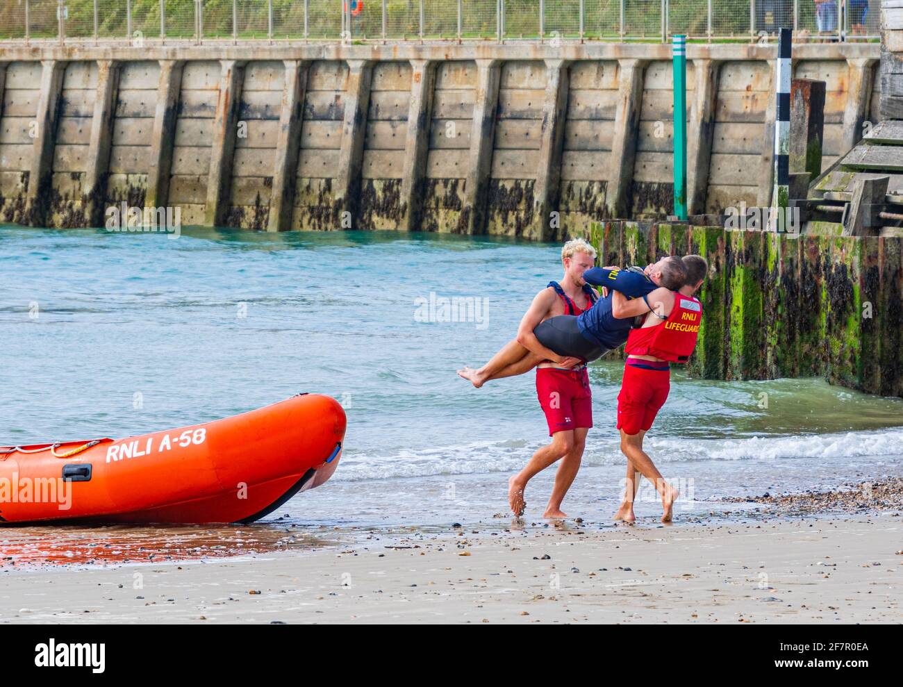 Bagnini che si allenano su una spiaggia, mostrando a qualcuno che gioca un paziente ferito che viene salvato e trasportato dal mare, nel Regno Unito. Foto Stock