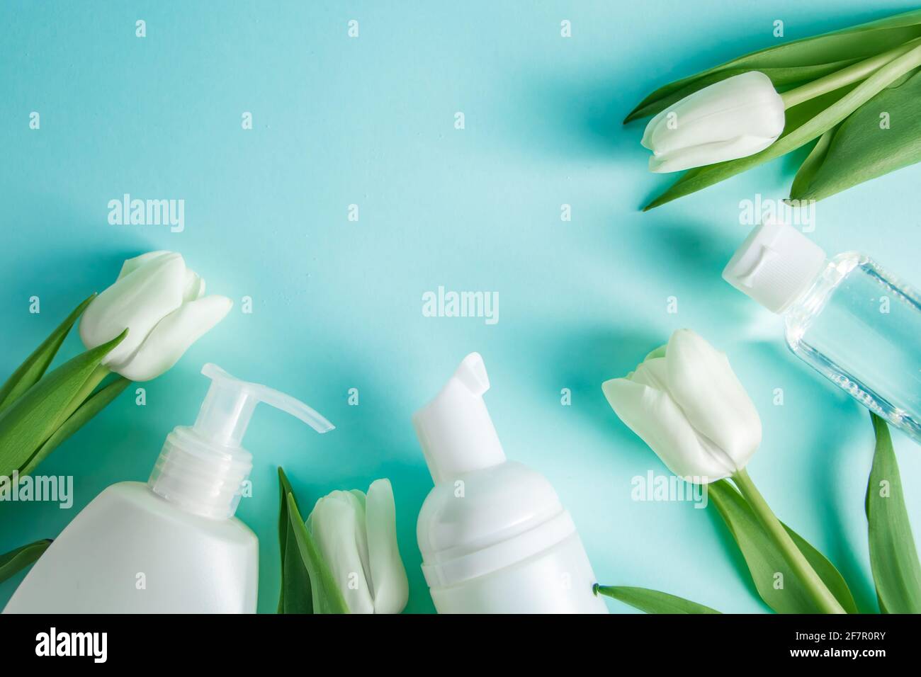 Prodotti per la cura della pelle su sfondo blu. Cosmetici naturali e tulipani bianchi. Posiziona per il testo. Foto Stock